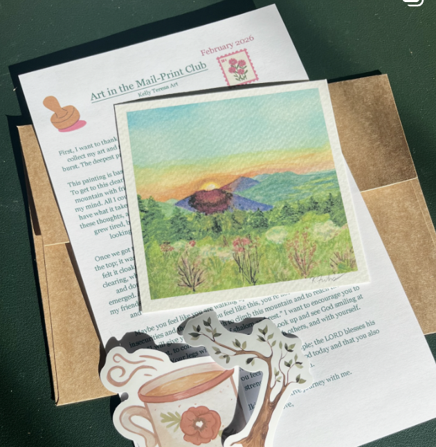 A postcard featuring a sunset or sunrise over a mountain landscape with colorful sky and green hills, decorated with a tree and a coffee cup sticker, placed on a piece of paper with printed text, atop a cardboard box.