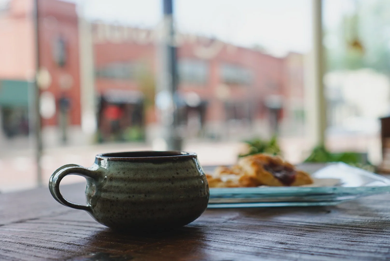 A ceramic mug and a plate with pastry on a wooden table near a window