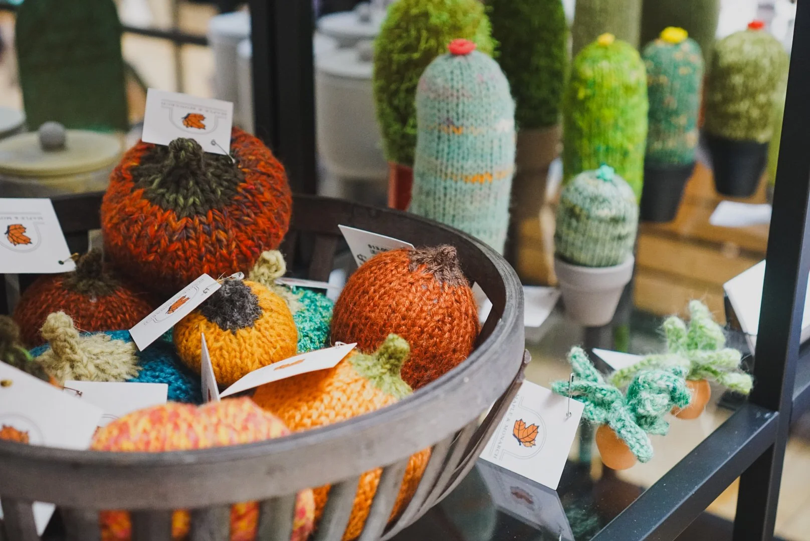 Display of colorful knitted accessories, clothing, and decorations in a store, including scarves, sweaters, hats, and cactus-shaped knitted pouches.