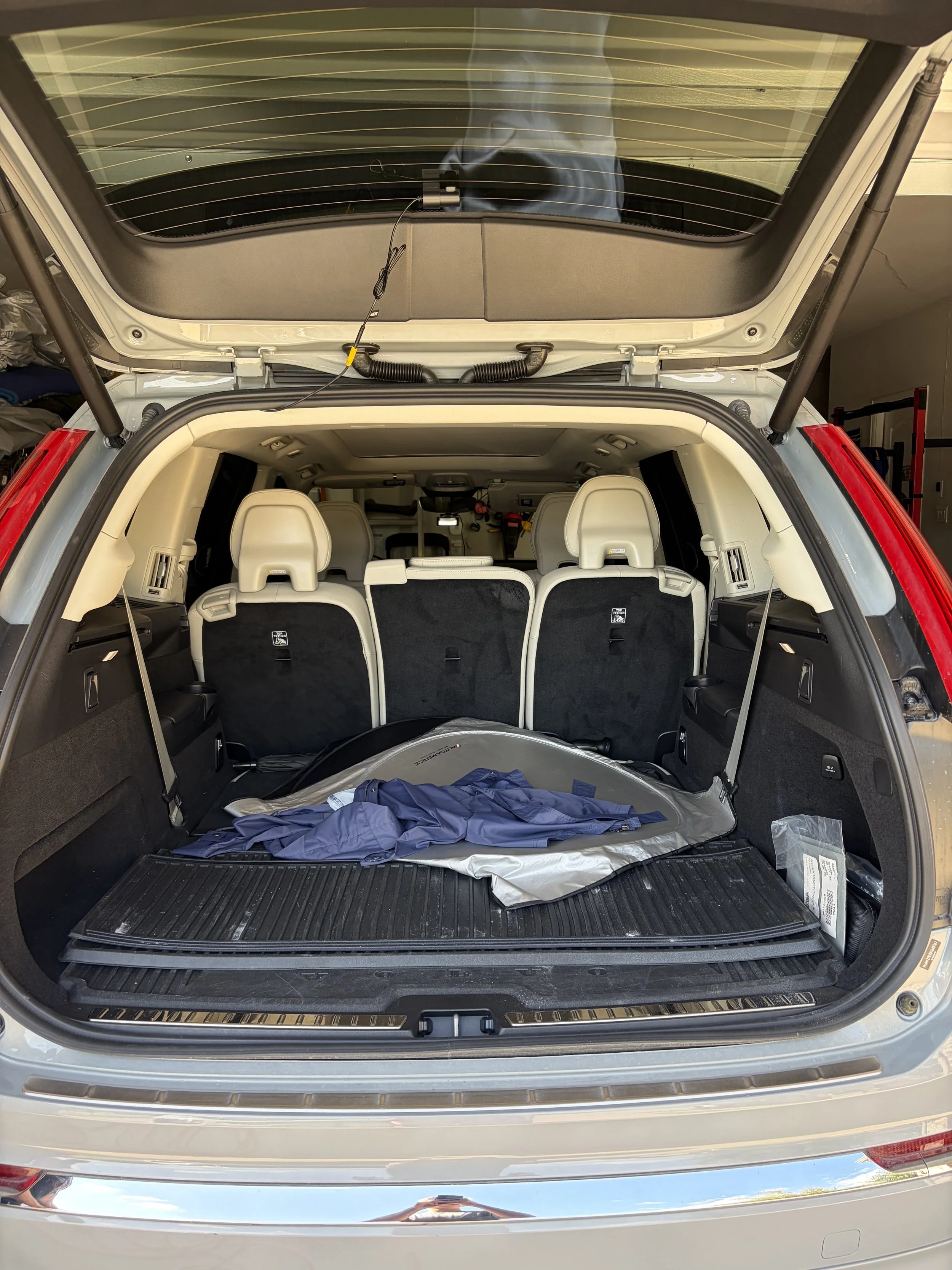 The open trunk of a silver SUV showing beige interior seats and a cargo area with a navy blue jacket and some items.