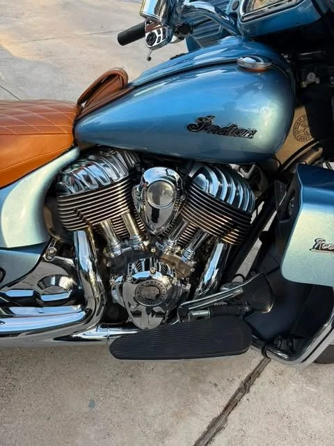 Close-up of a motorcycle with a blue fuel tank, chrome engine parts, and a tan leather seat.
