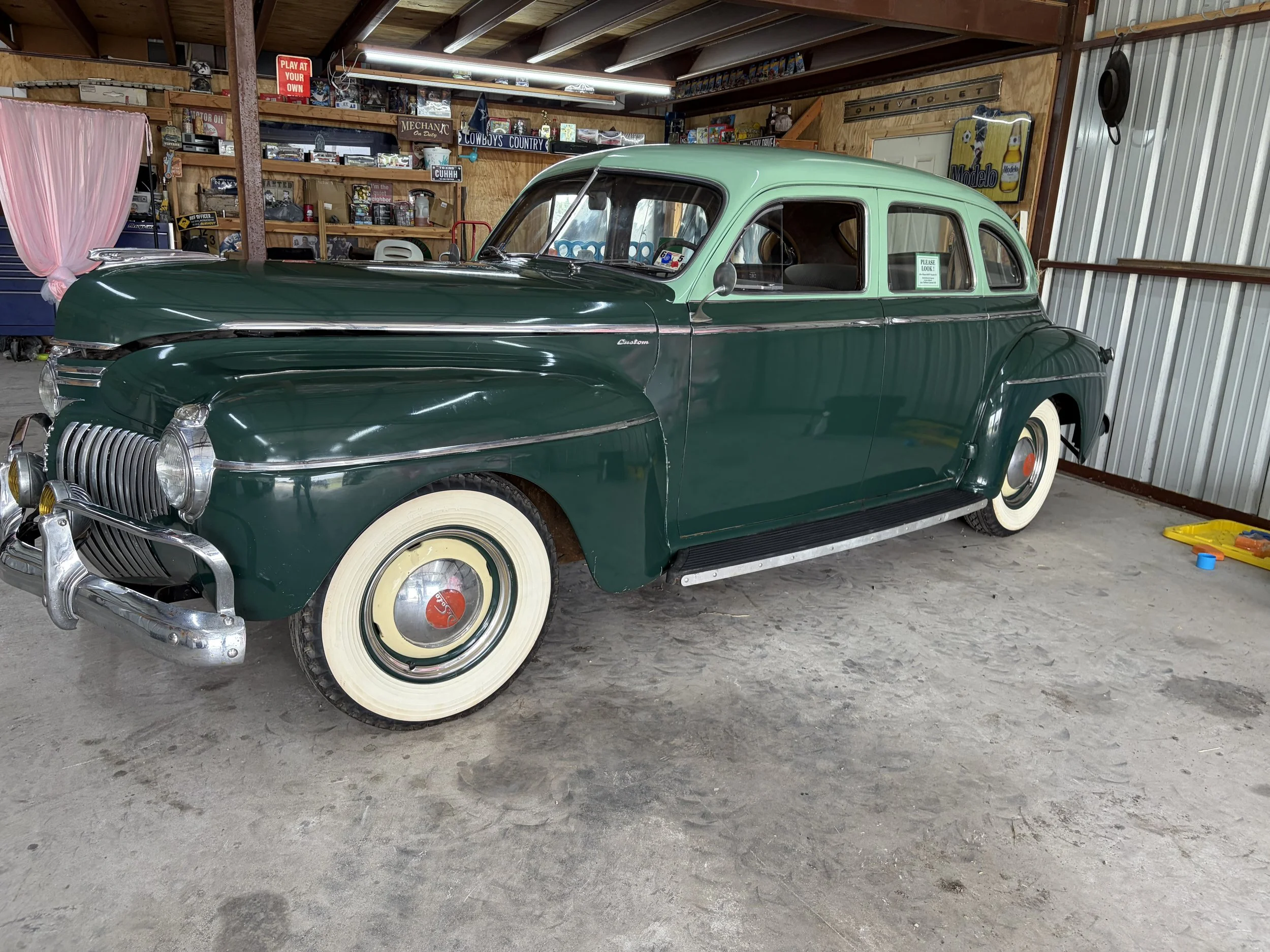 A vintage green car with whitewall tires parked inside a cluttered garage.
