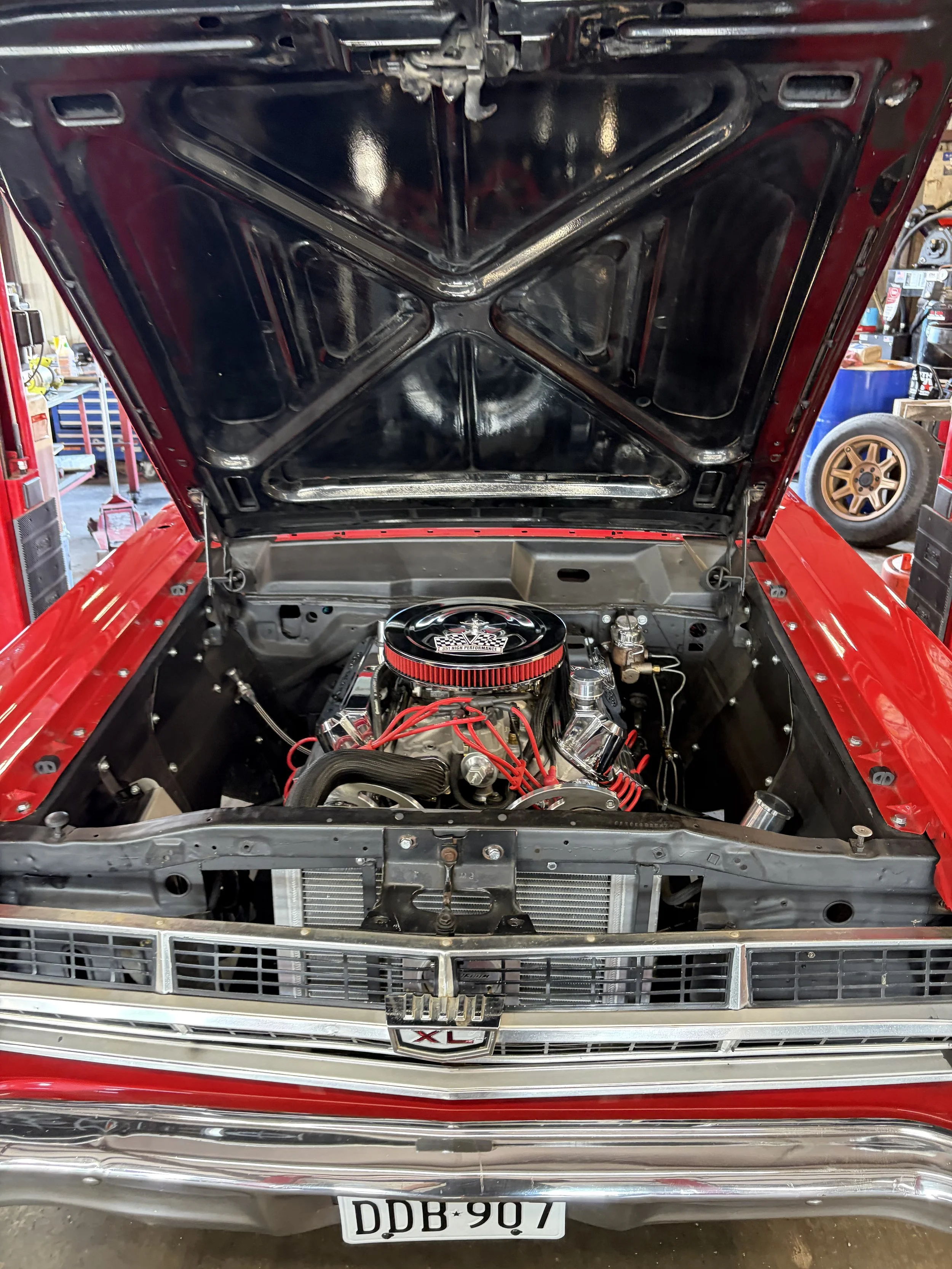 Front view of a vintage red car with its hood open, exposing the engine and engine bay, with a chrome grille, badge reading 'XL,' and a license plate 'DDB 907'.