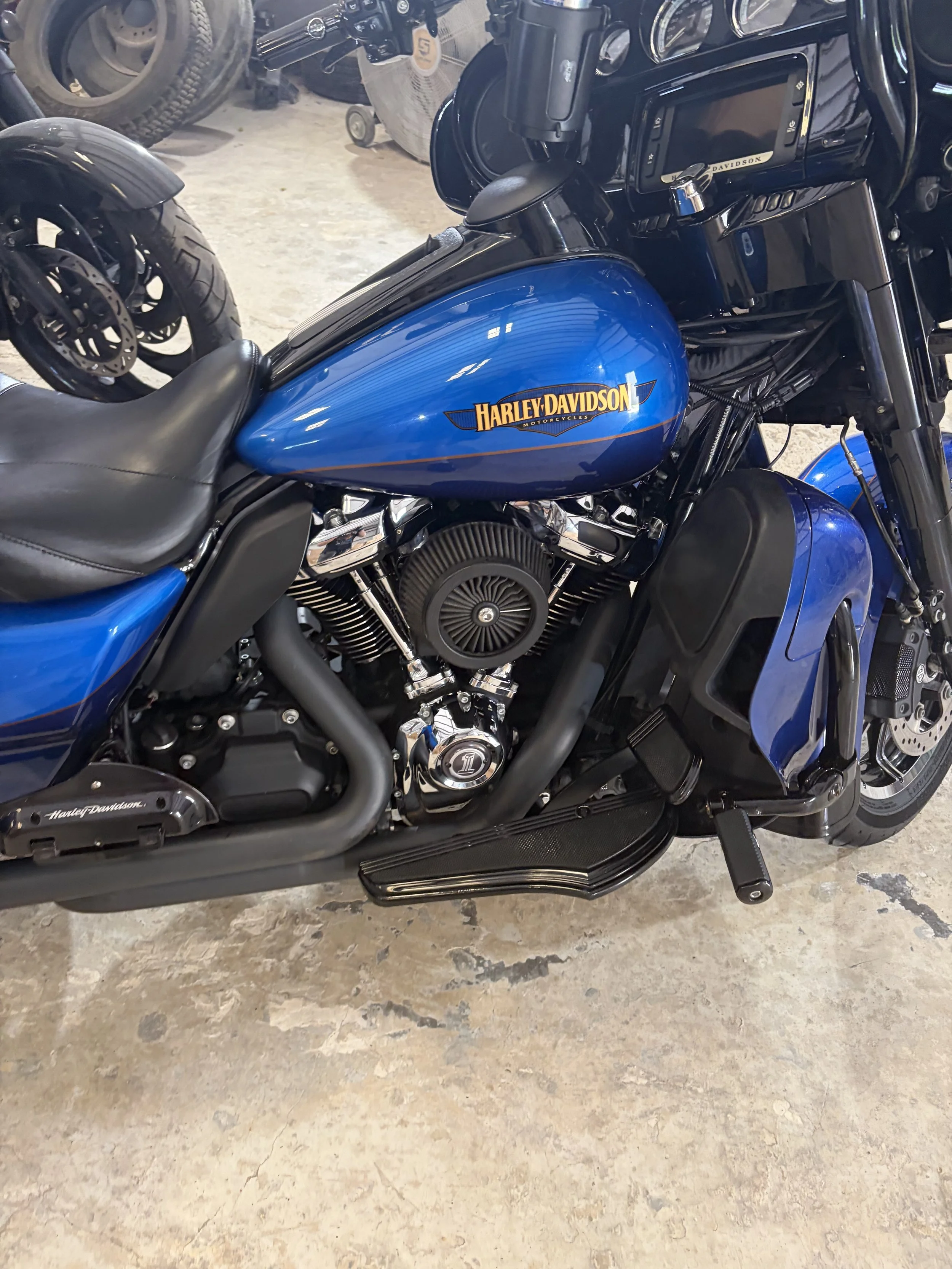 A blue Harley Davidson motorcycle parked on a concrete floor, showing the gas tank, seat, and engine components.