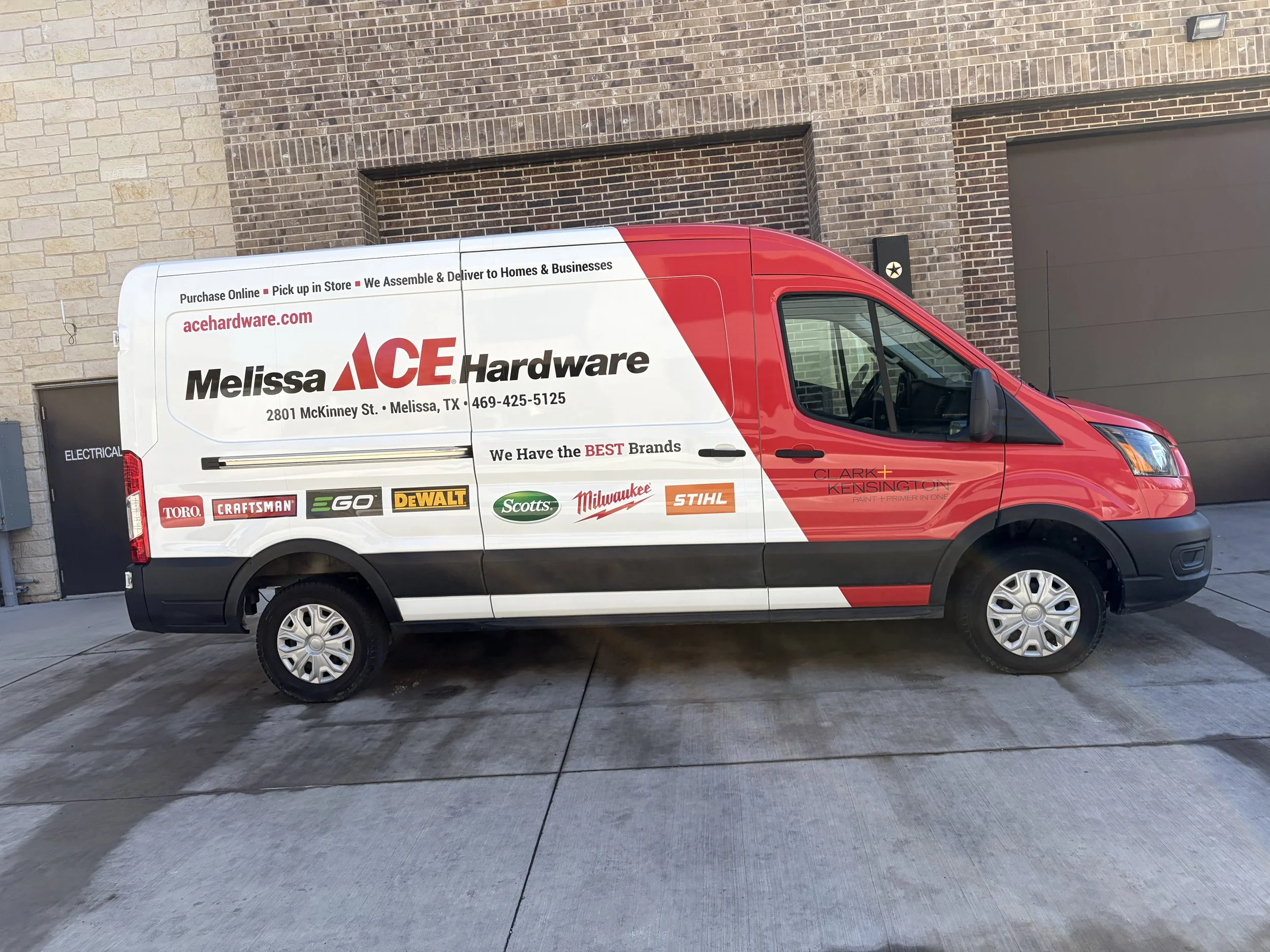 Red and white delivery van with company branding, parked in front of a brick building with garage doors.
