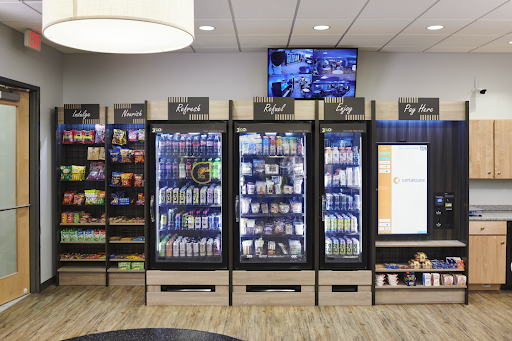 Vending machines with snacks, drinks, and a touchscreen for payments in a break room.
