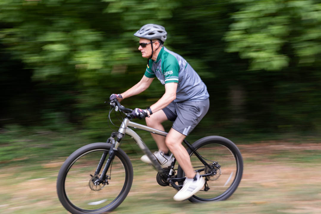 Man riding a mountain bike through a wooded area wearing a helmet and sunglasses.