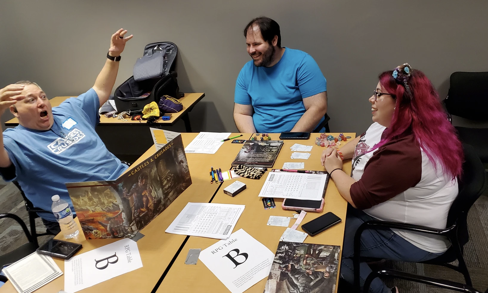 Three people sitting at a table playing a tabletop role-playing game, with character sheets, dice, and game materials.