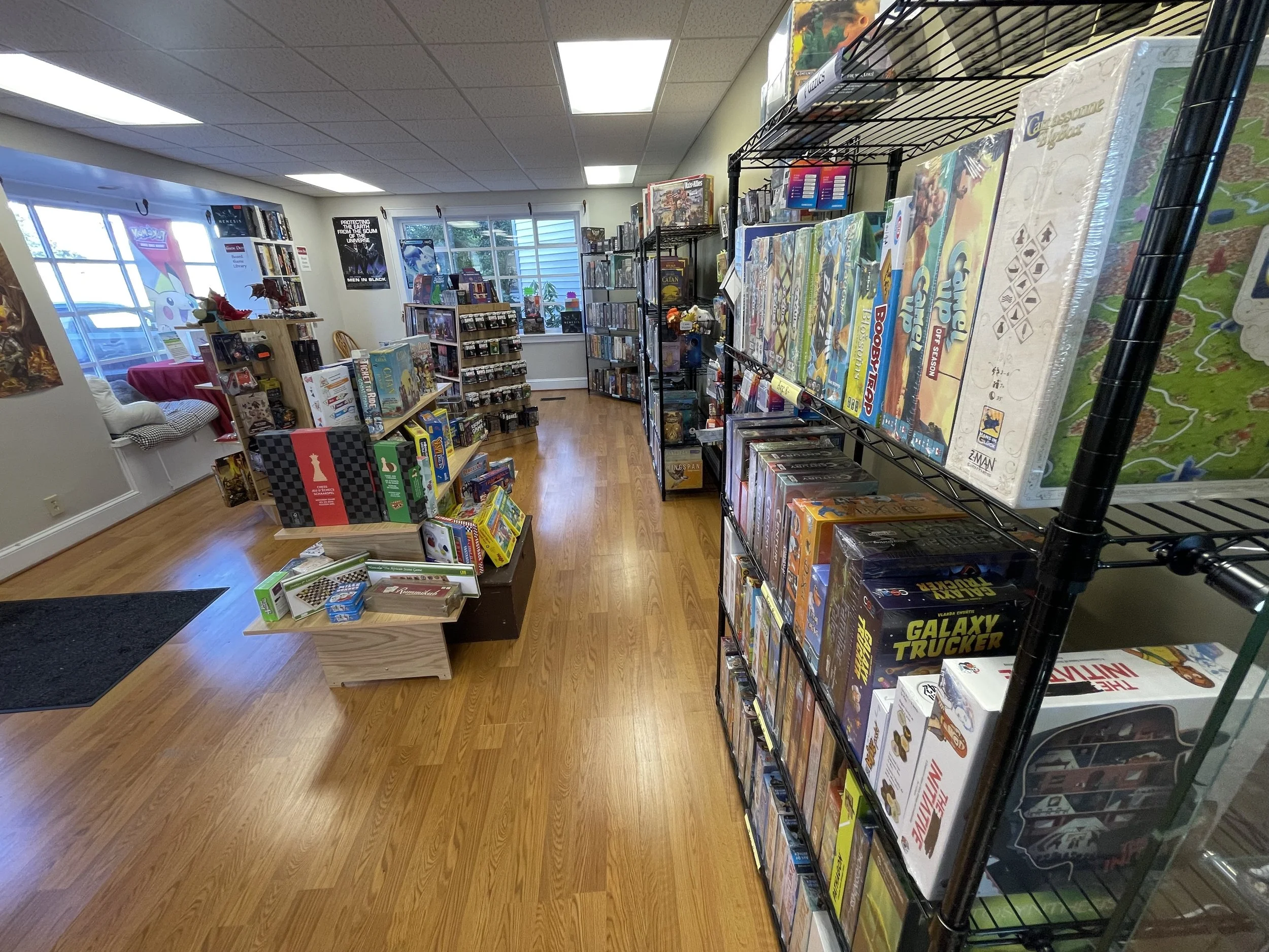 Interior of a game store with shelves of board games and puzzles, wooden floors, and windows letting in natural light.