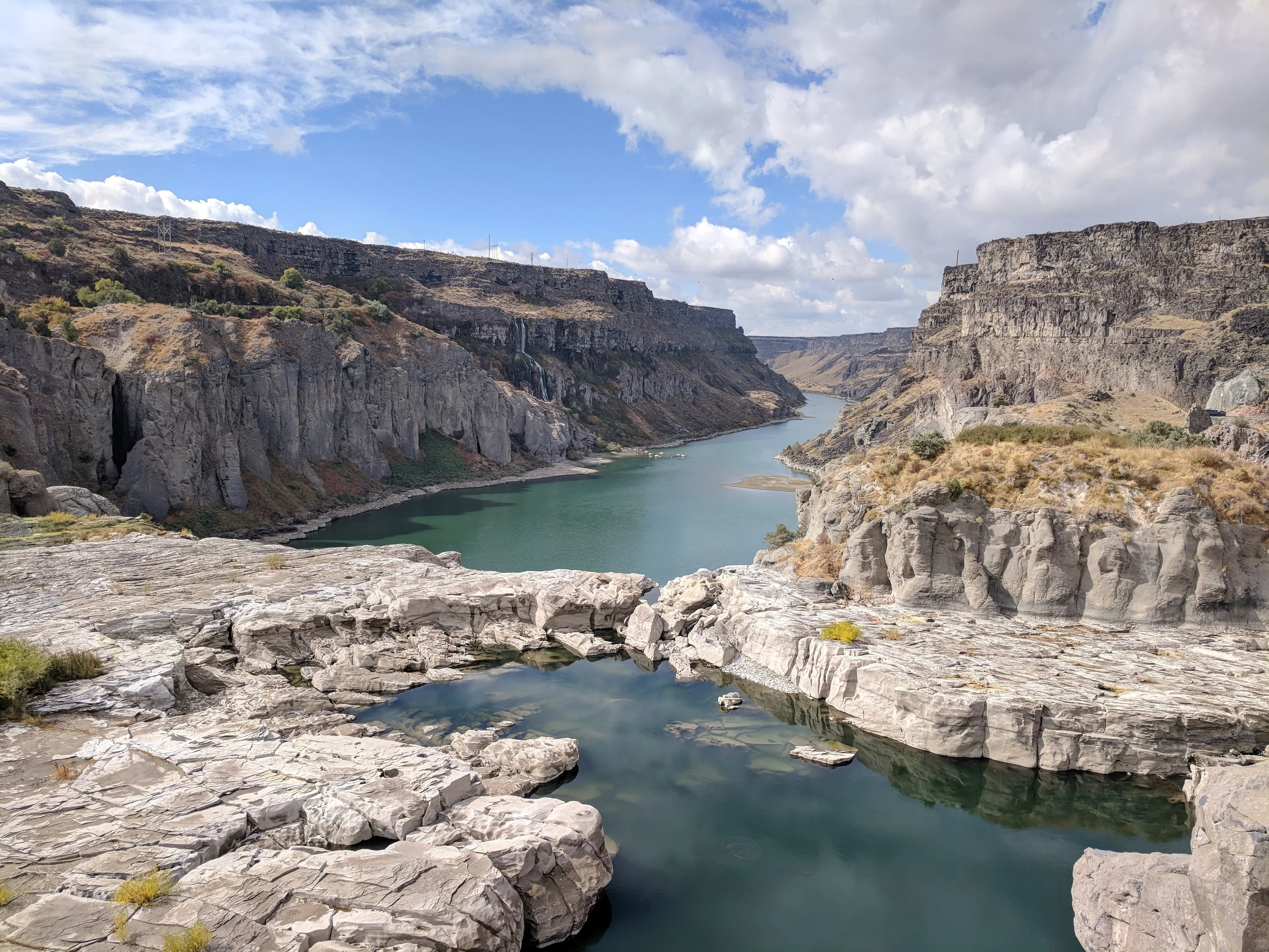 A deep canyon with steep, rocky walls and a river winding through it, under a partly cloudy sky.