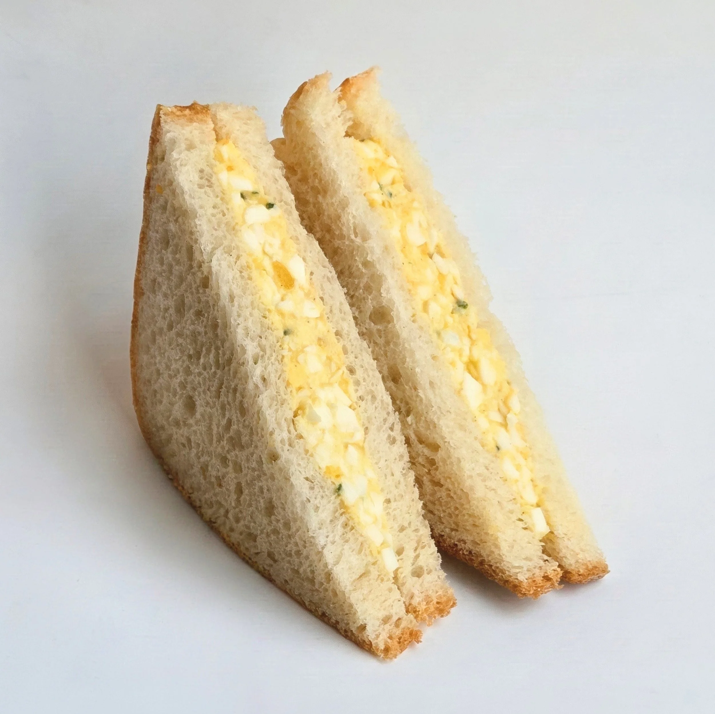 Two slices of egg salad sandwich on white bread with a plain white background.