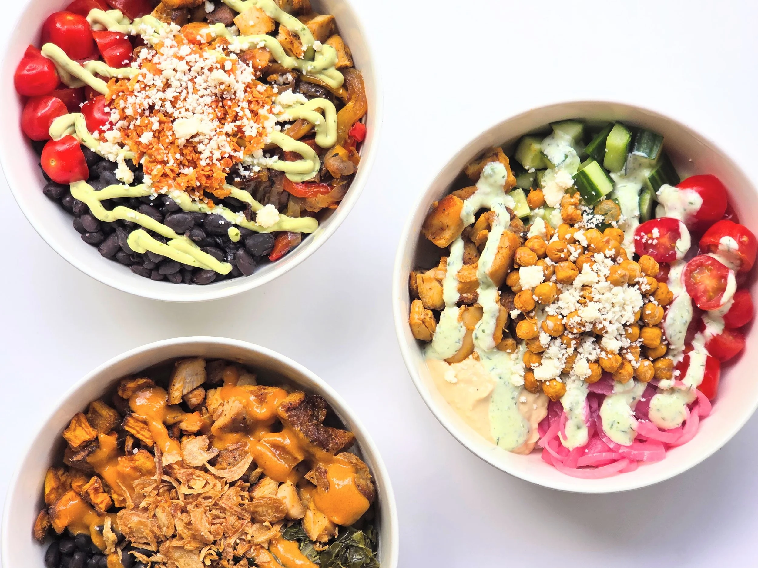 Three bowls of colorful salads with beans, vegetables, shredded cheese, and drizzled dressing, arranged on a white surface.