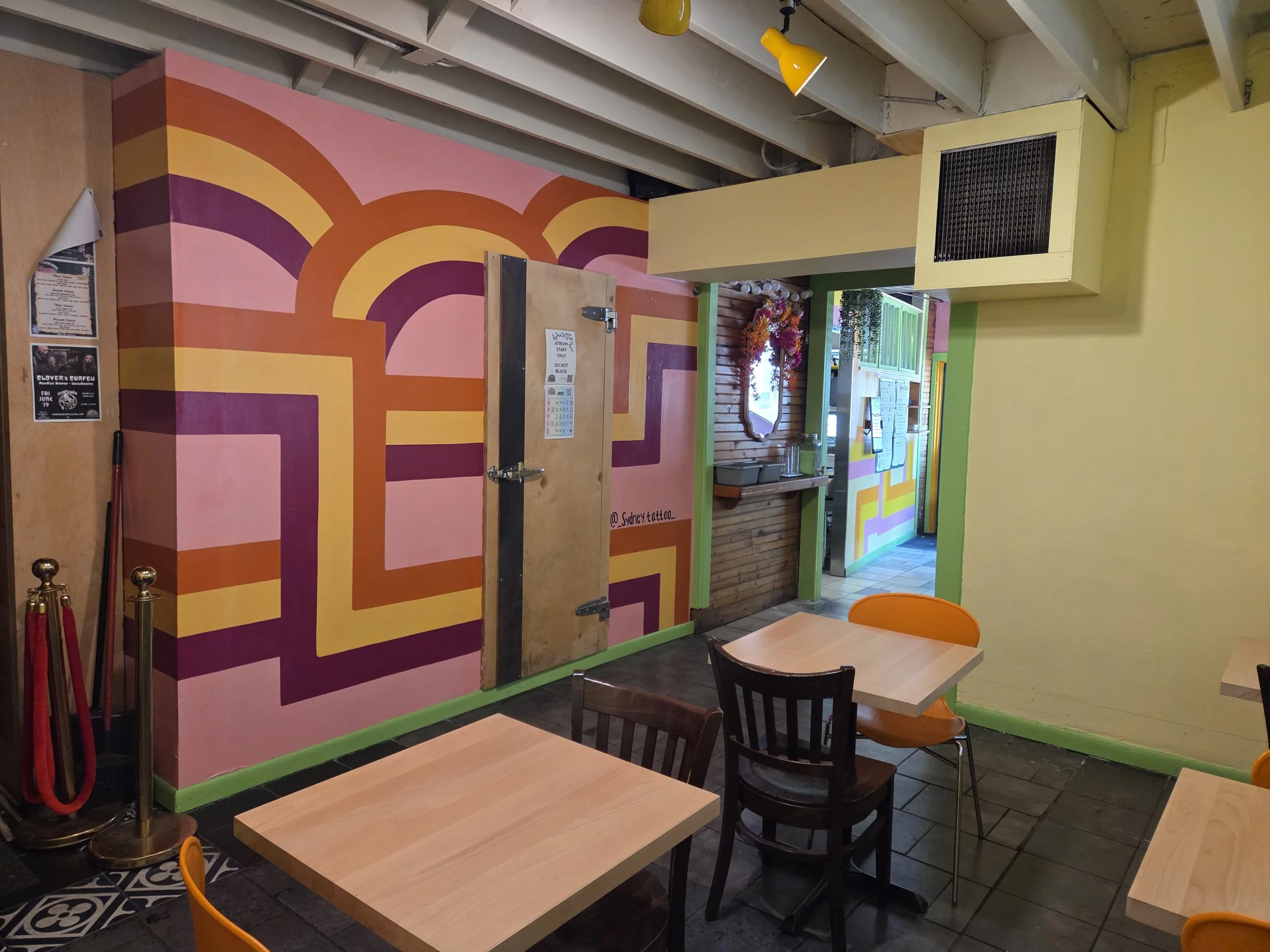 Interior of a colorful restaurant with patterned wall, potted flowers, and wooden tables and chairs.