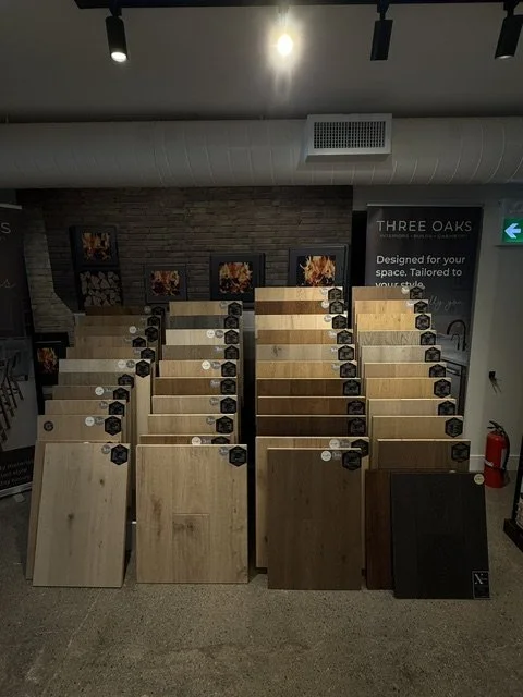 Display of wood flooring samples arranged in rows in a store, with a brick wall and framed pictures in the background.