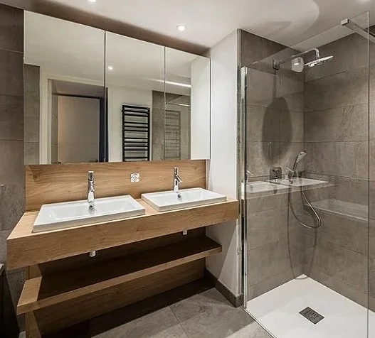 Modern bathroom with dual sinks on a wooden vanity, large mirrored cabinet, and a glass-enclosed shower with gray tiles.