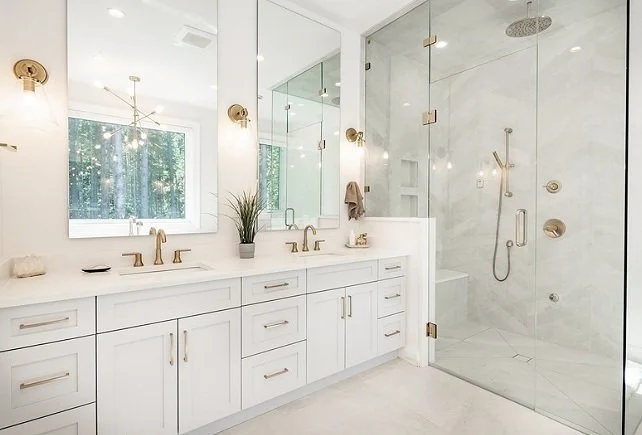 Modern bathroom with white vanity, large mirror, gold fixtures, and a glass-enclosed shower with multiple showerheads.