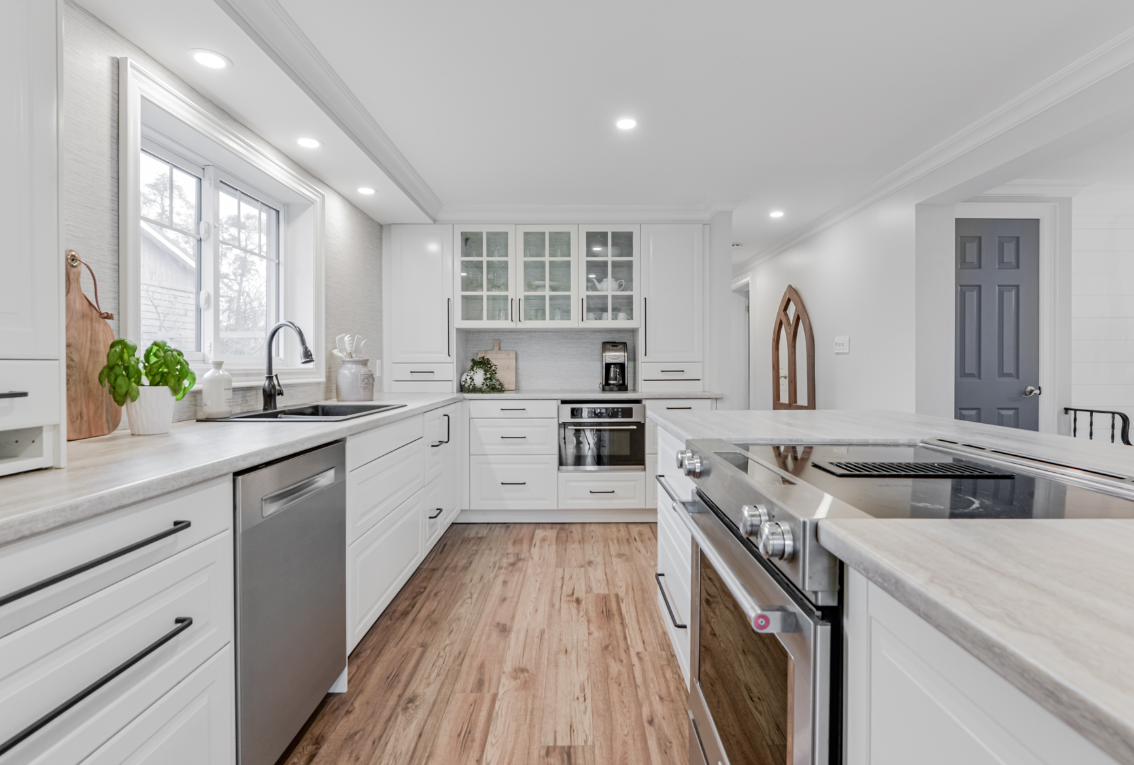 Modern kitchen with white cabinets, a window above the sink, stainless steel appliances, light wood flooring, and decorative items on the counter.
