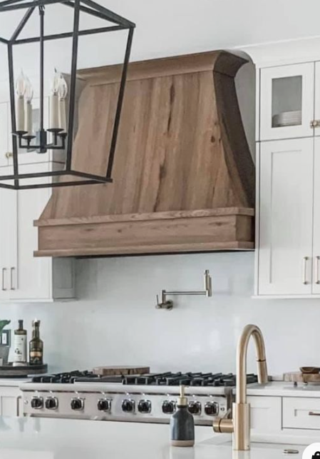 Kitchen with white cabinets, a wooden range hood, a modern faucet, and a black chandelier.