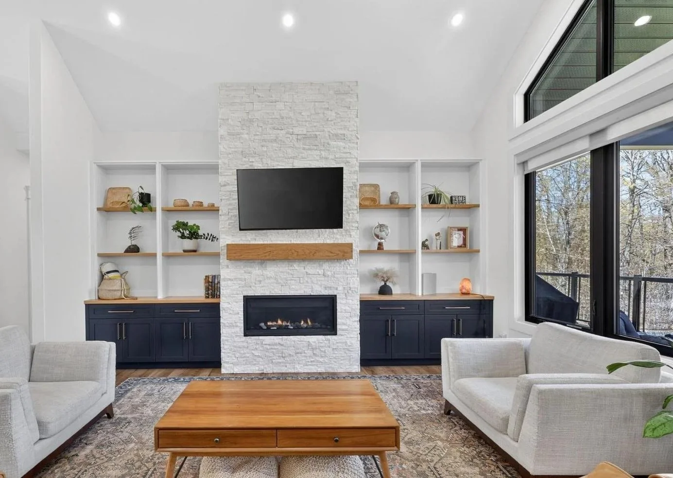 Living room with white walls, large windows, built-in shelves, a fireplace, and a flat-screen TV above the fireplace.