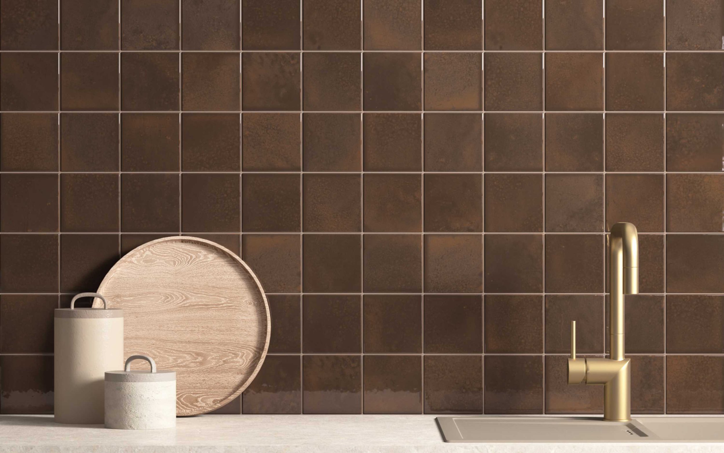 Kitchen countertop with a black tiled wall, a brass faucet, and two rolled paper towels next to a wooden tray and a small white container.