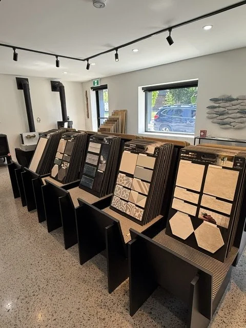 Interior of a flooring showroom displaying sample tiles and wood flooring options on black display panels.