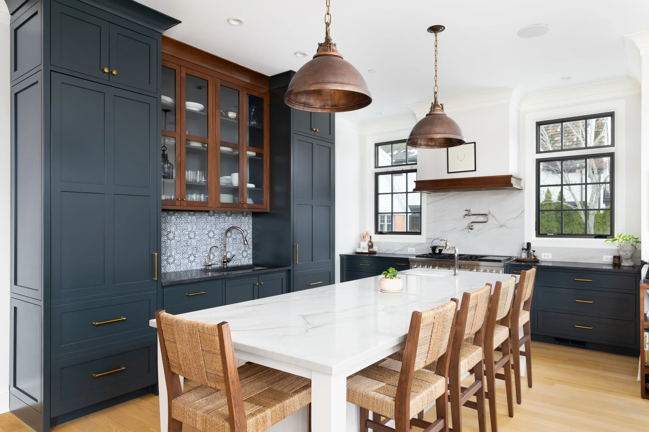 Modern kitchen with navy blue cabinets, white marble island, and natural wood dining chairs.
