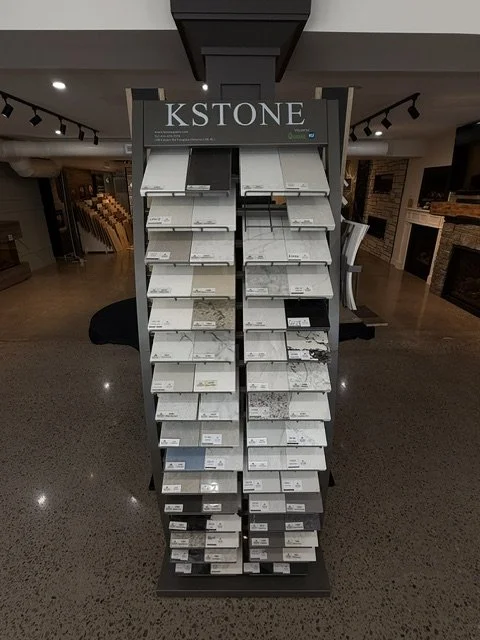 Display stand with samples of natural stone slabs, labeled 'KSTONE', showcasing various colors and textures for countertops or flooring.