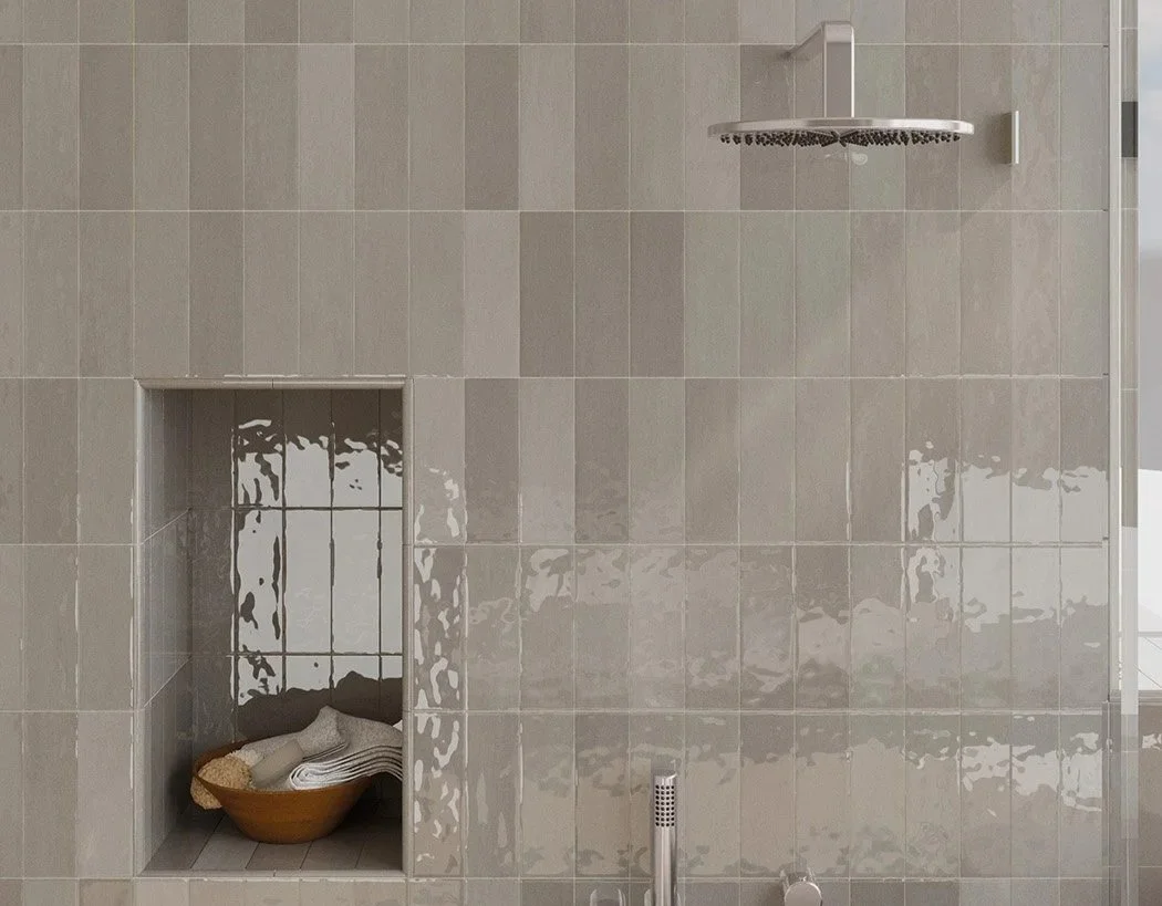 A shower with beige tiles, a showerhead on the ceiling, a built-in nook holding rolled towels, and a window with a grid pattern in the background.