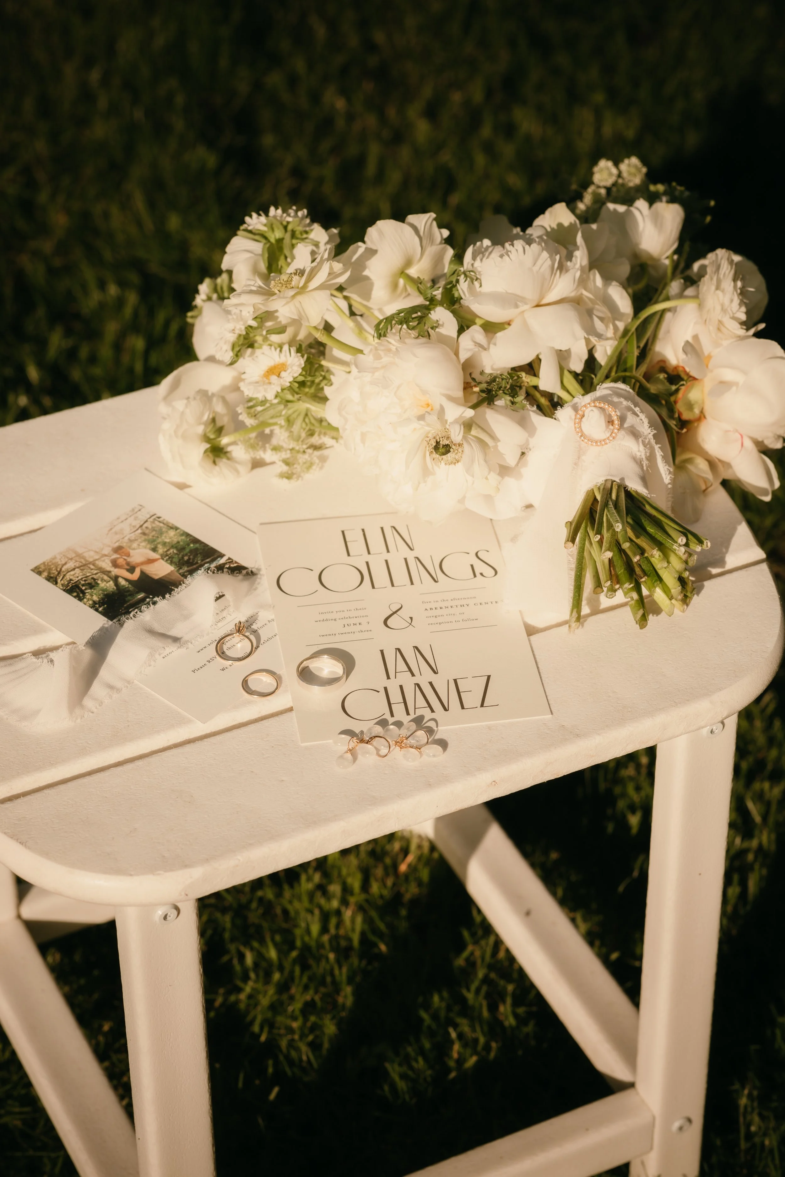 White flowers arranged on a table with wedding rings and wedding invitation cards.