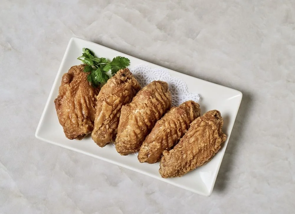 Six pieces of fried chicken on a white rectangular plate garnished with cilantro leaves.