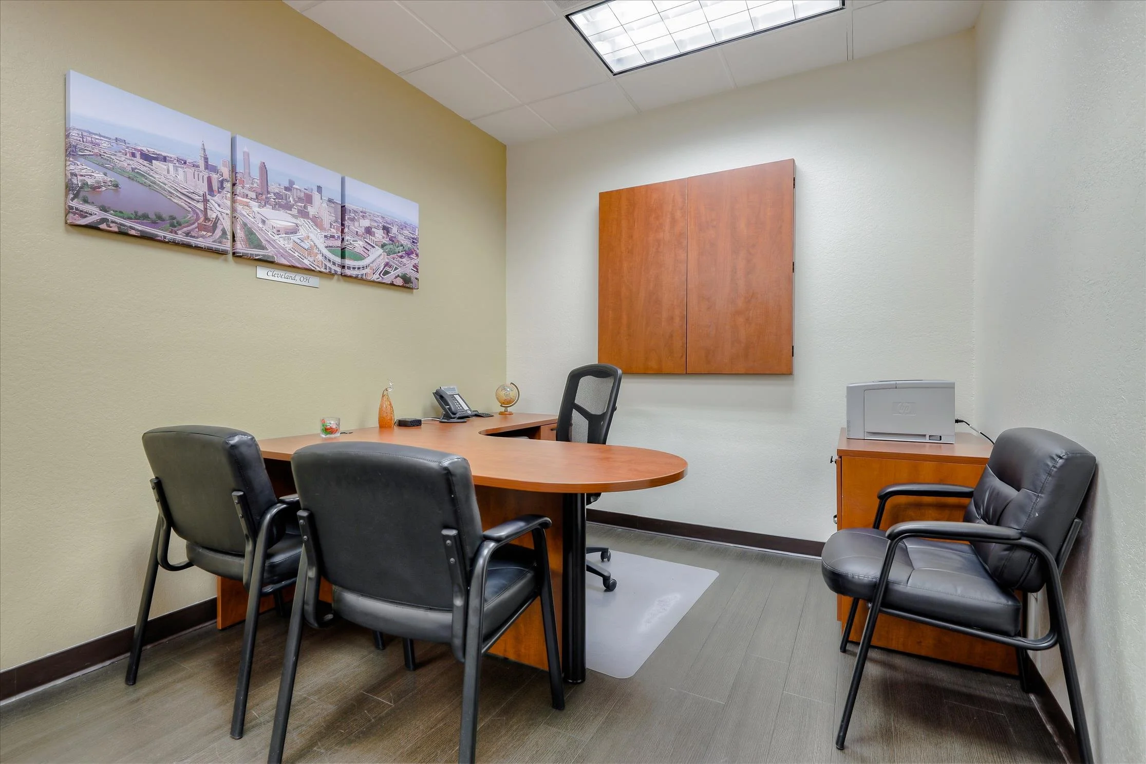 An office conference room with a wooden table, black chairs, and wall decorations including a cityscape photograph of Cleveland, Ohio.