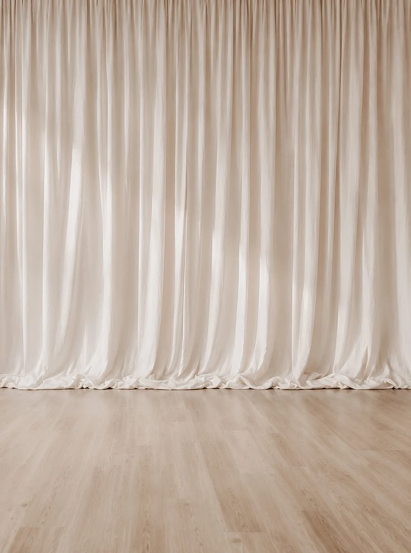 A large beige curtain hanging from ceiling to floor in front of a light wood floor.
