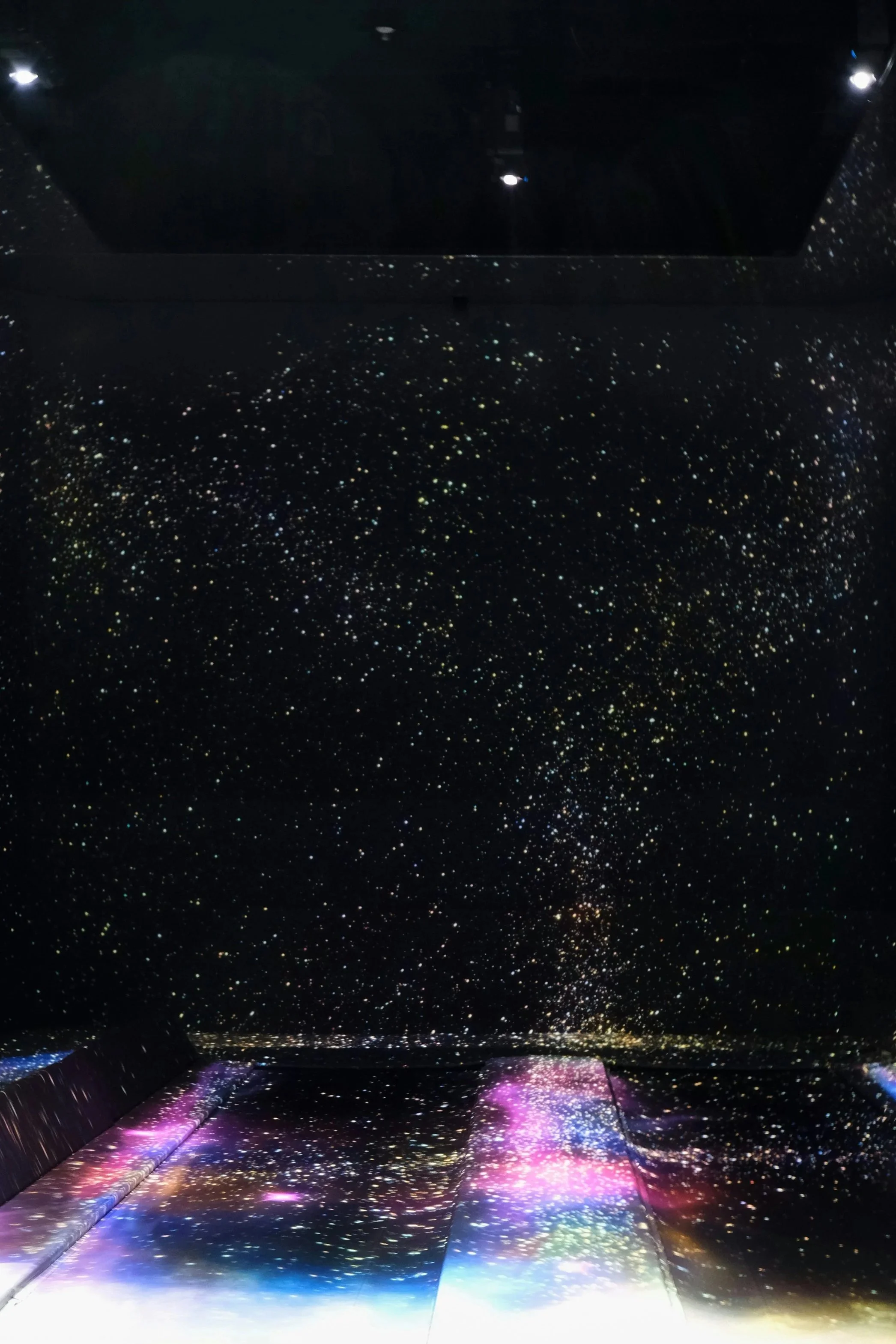 A dark room with a starry sky pattern projected on the walls and floor, creating the illusion of being in space.