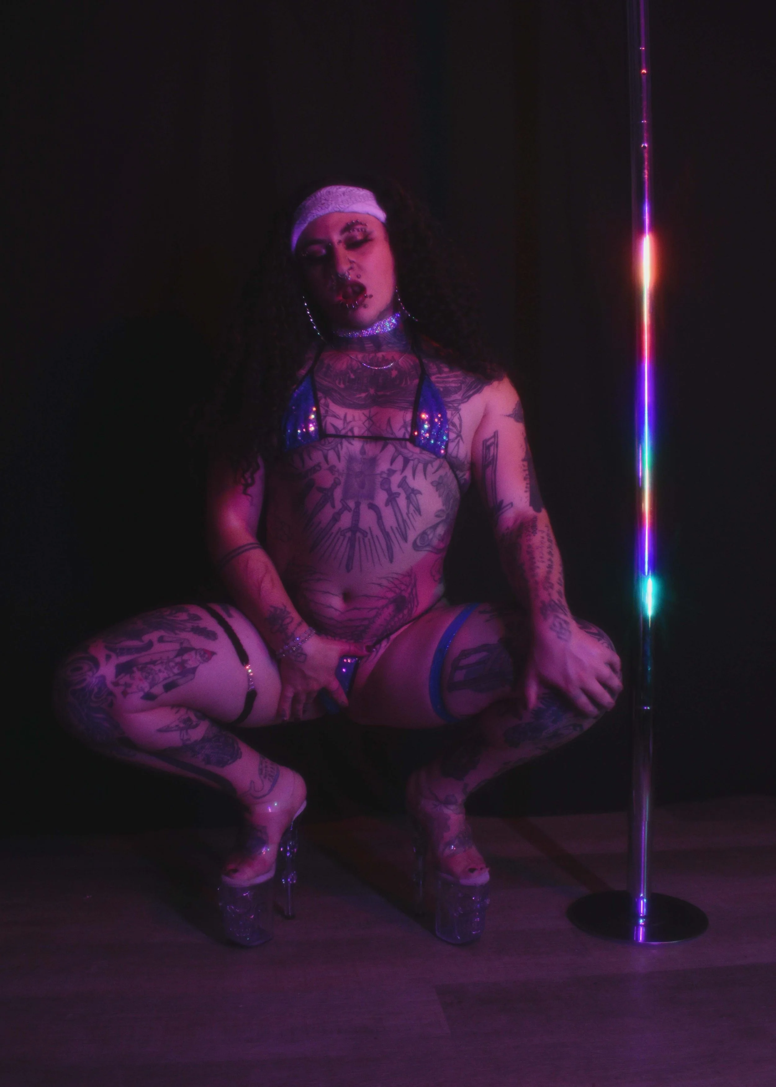 A non binary trans queer stripper wearing high-heeled shoes, with numerous tattoos covering their body, wearing a white headband, jewelry, and a revealing outfit, near a neon pole. pole dancer, lgbt stripper lgbt friendly adult entertainment erotic