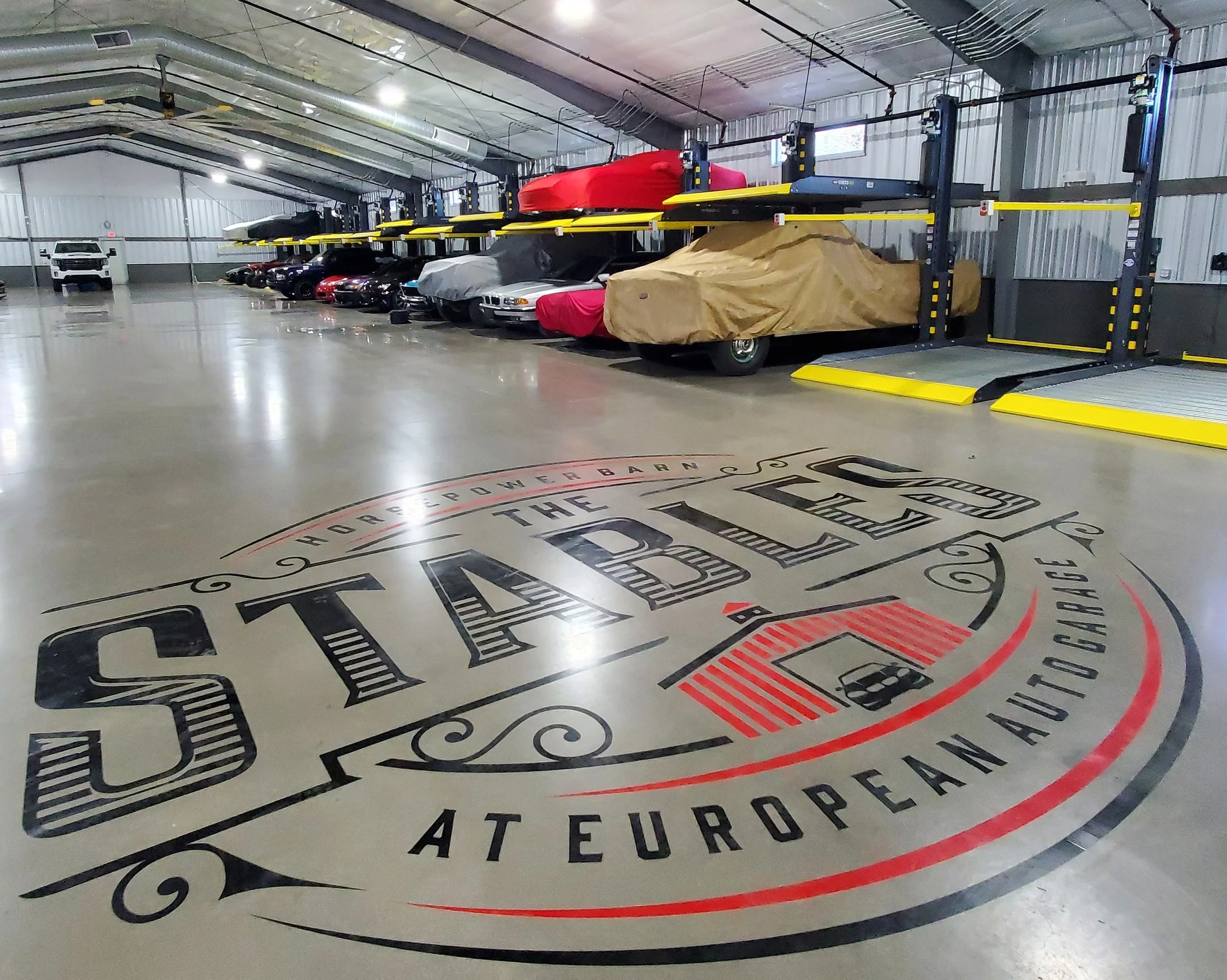 Underground parking garage with cars covered in protective covers and a large circular sign on the floor that reads "The Power of the Car"