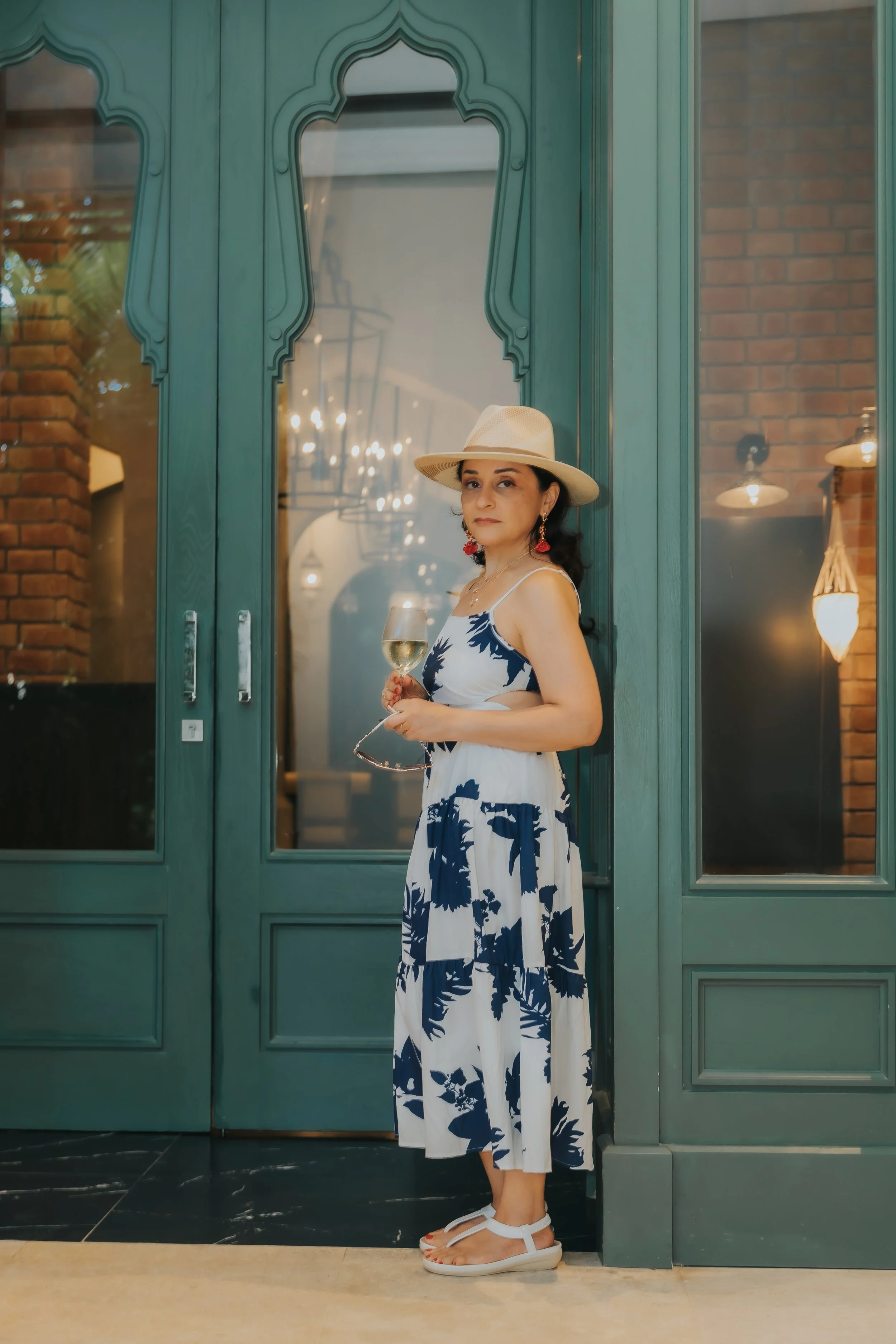 Tania Lopez holding a glass of wine in front of elegant green architectural doors.