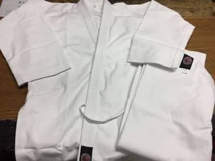 A white martial arts gi laid out on a wooden surface.
