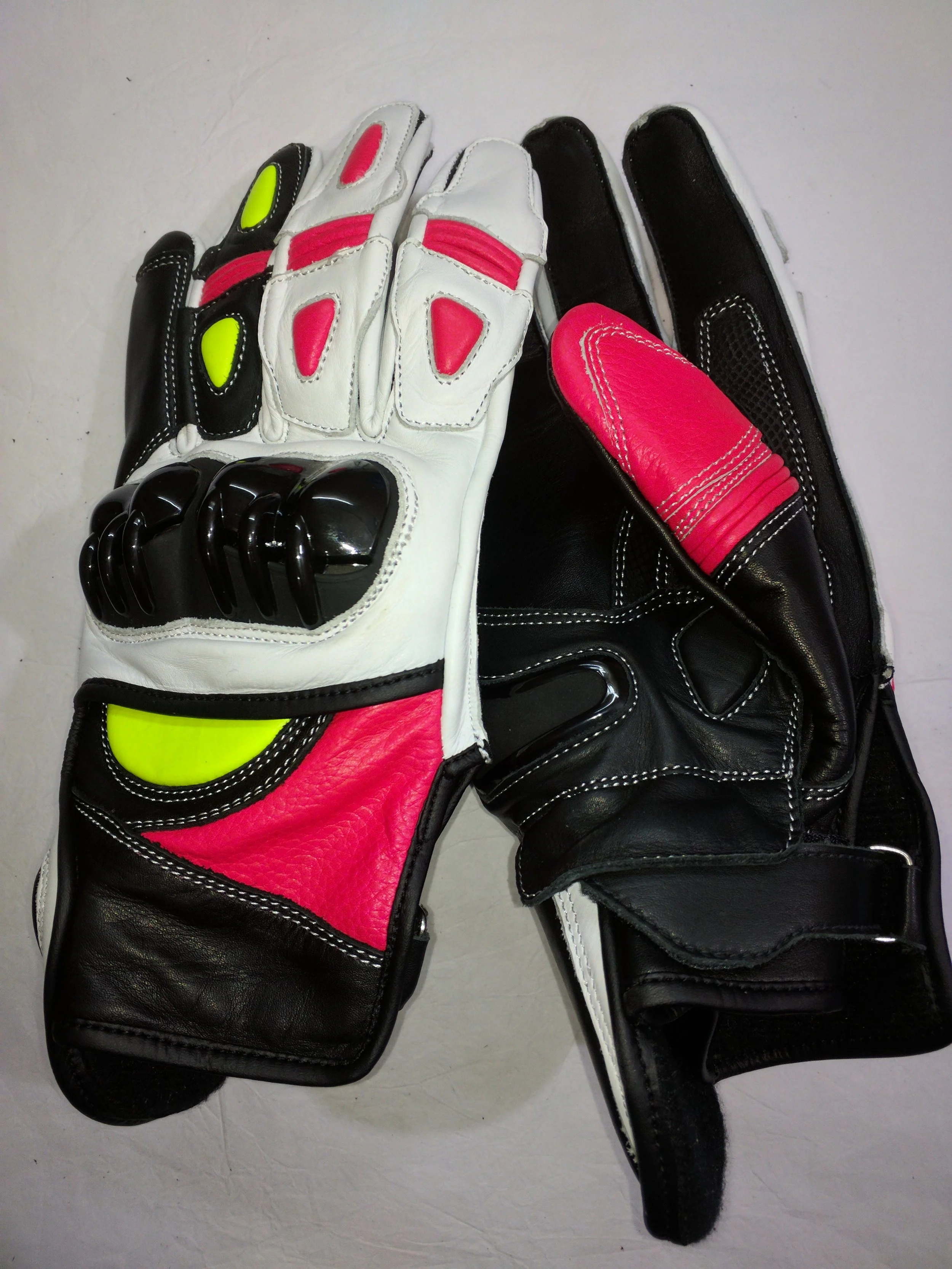 A pair of motorcycle gloves, one white with pink and black accents, and the other black with pink accents, placed on a white surface.