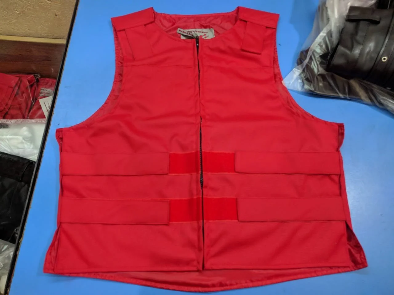 Red tactical or safety vest with a front zipper, laid flat on a blue surface.