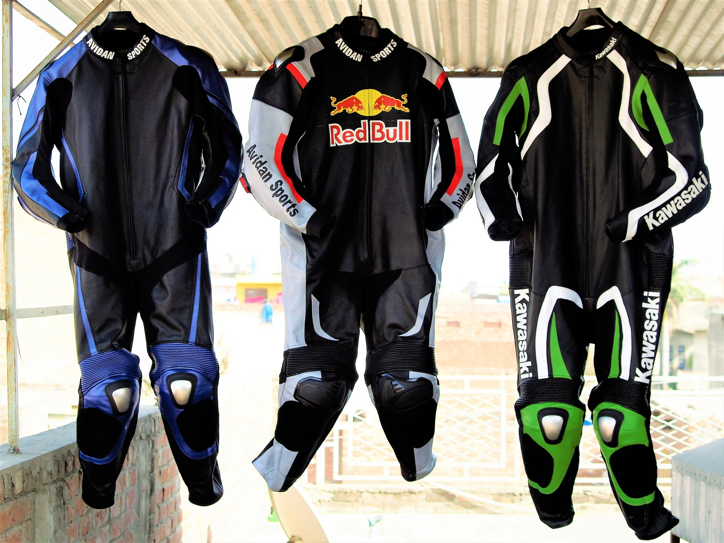 Three motorcycle racing suits hanging on a rack, with a roofed background.