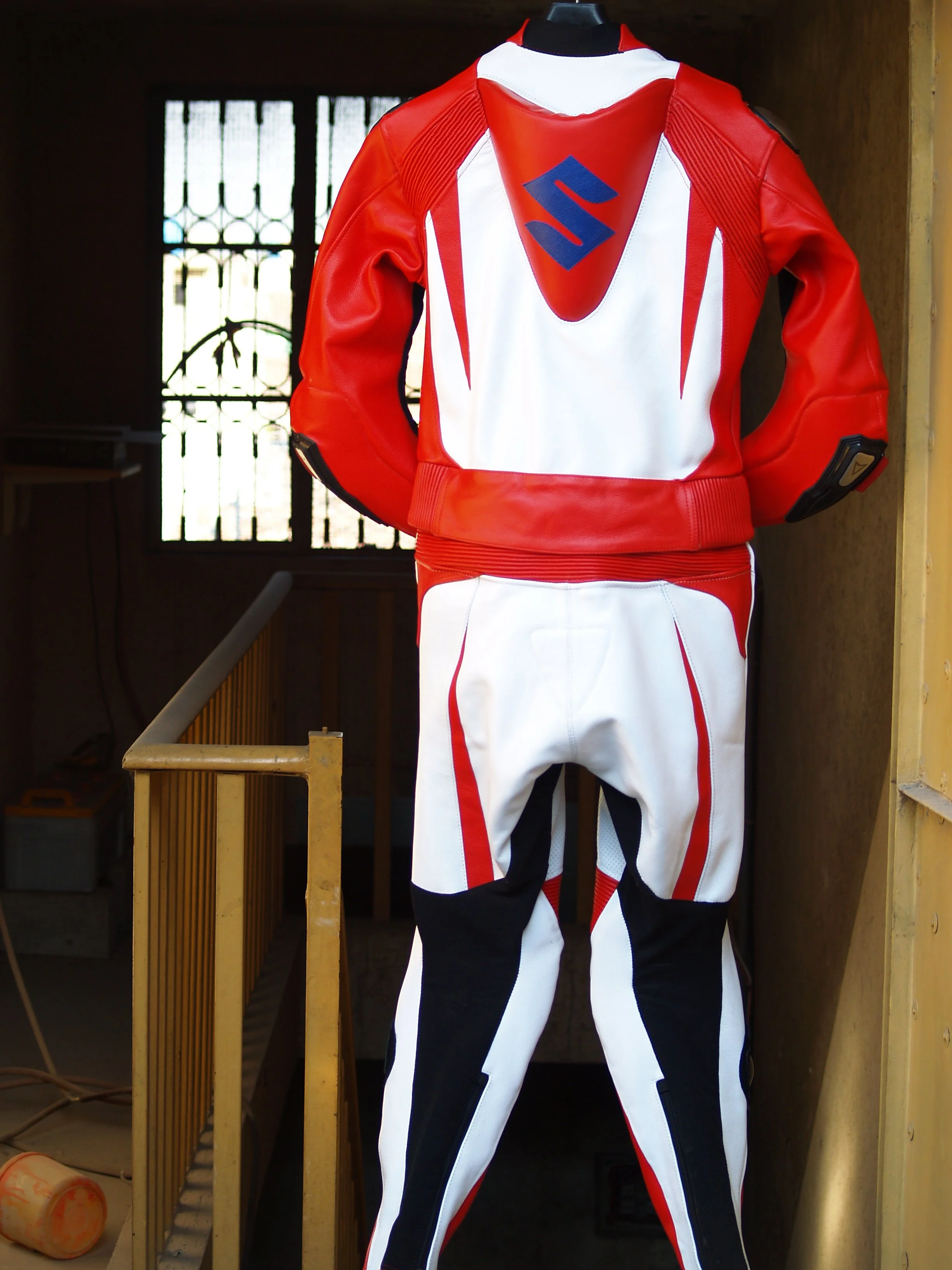 A red, white, and black motorcycle racing suit displayed on a mannequin in front of a window with security bars.