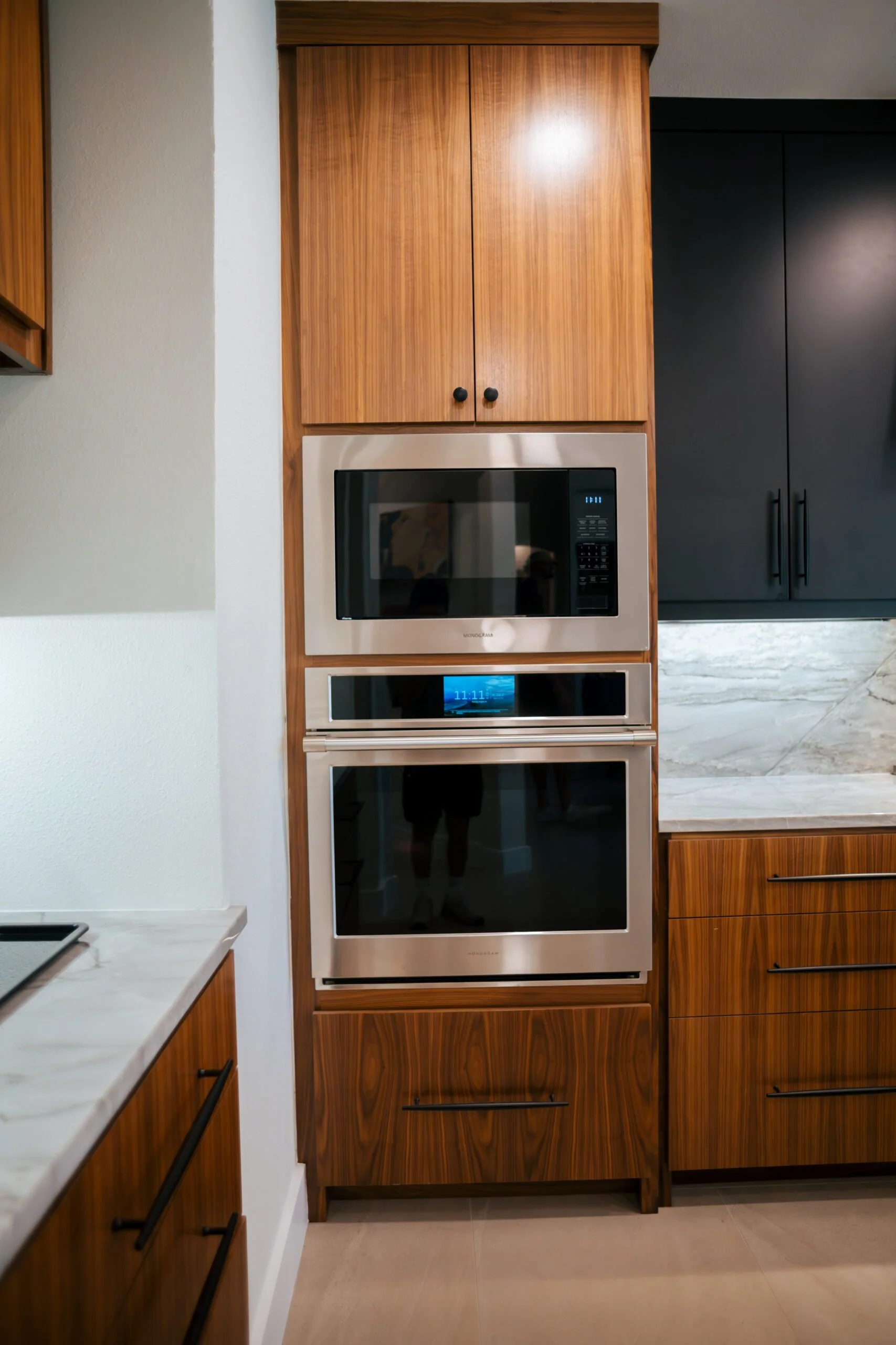 Kitchen with wooden cabinets, stainless steel microwave and oven, white marble countertop, and beige tile floor.