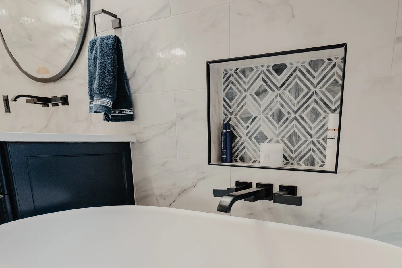 Modern bathroom with a marble wall, built-in shower niche with patterned tiles, black fixtures, and a blue towel hanging on a black towel bar