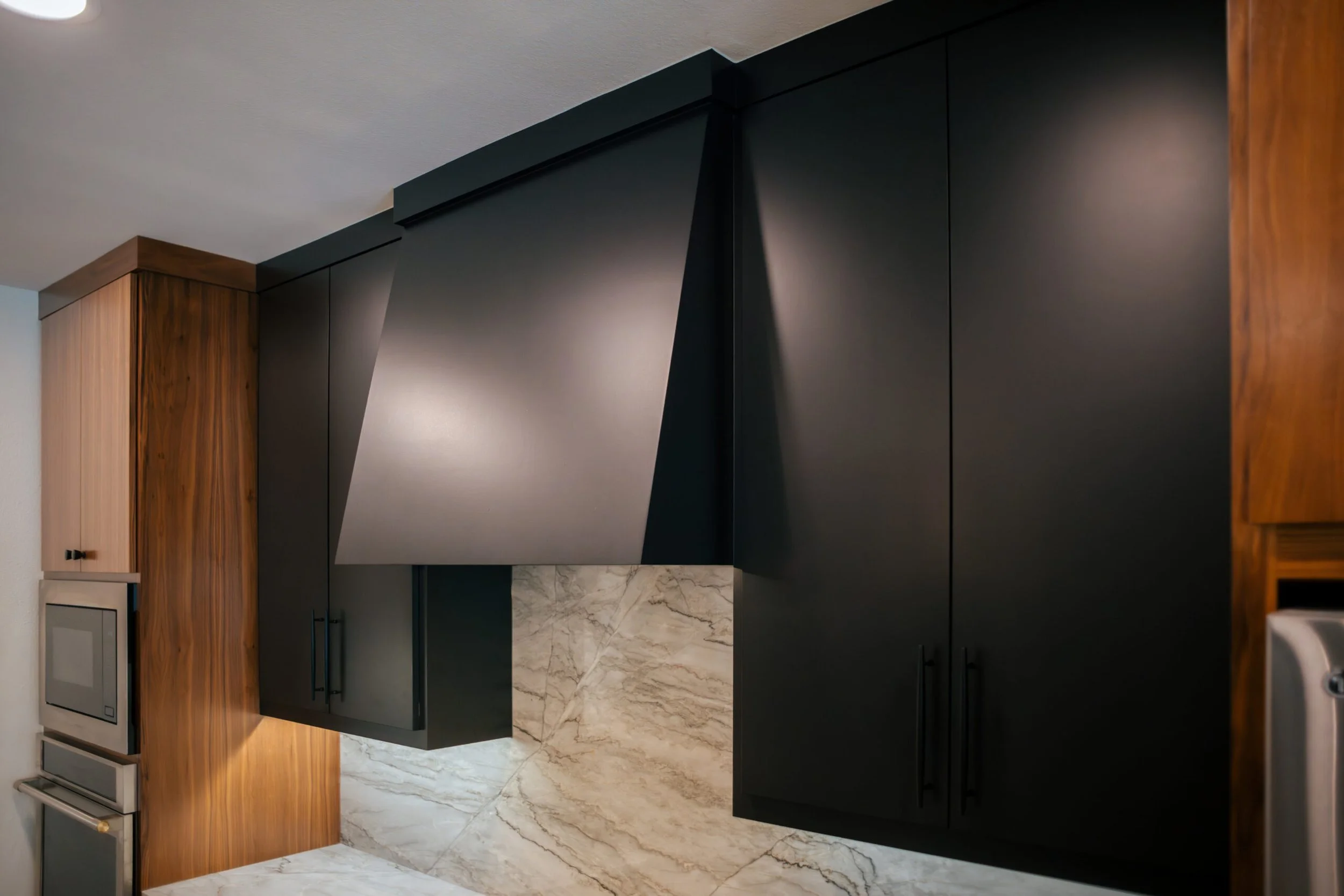 Modern kitchen with black cabinetry, wood accents, marble countertops, and marble flooring.
