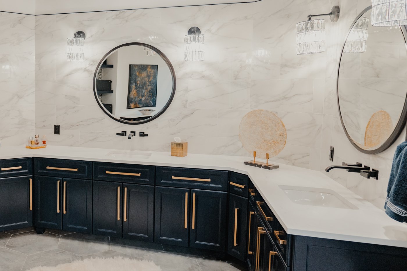 Modern bathroom with white marble walls, black cabinets, oval mirrors, and lighting fixtures.