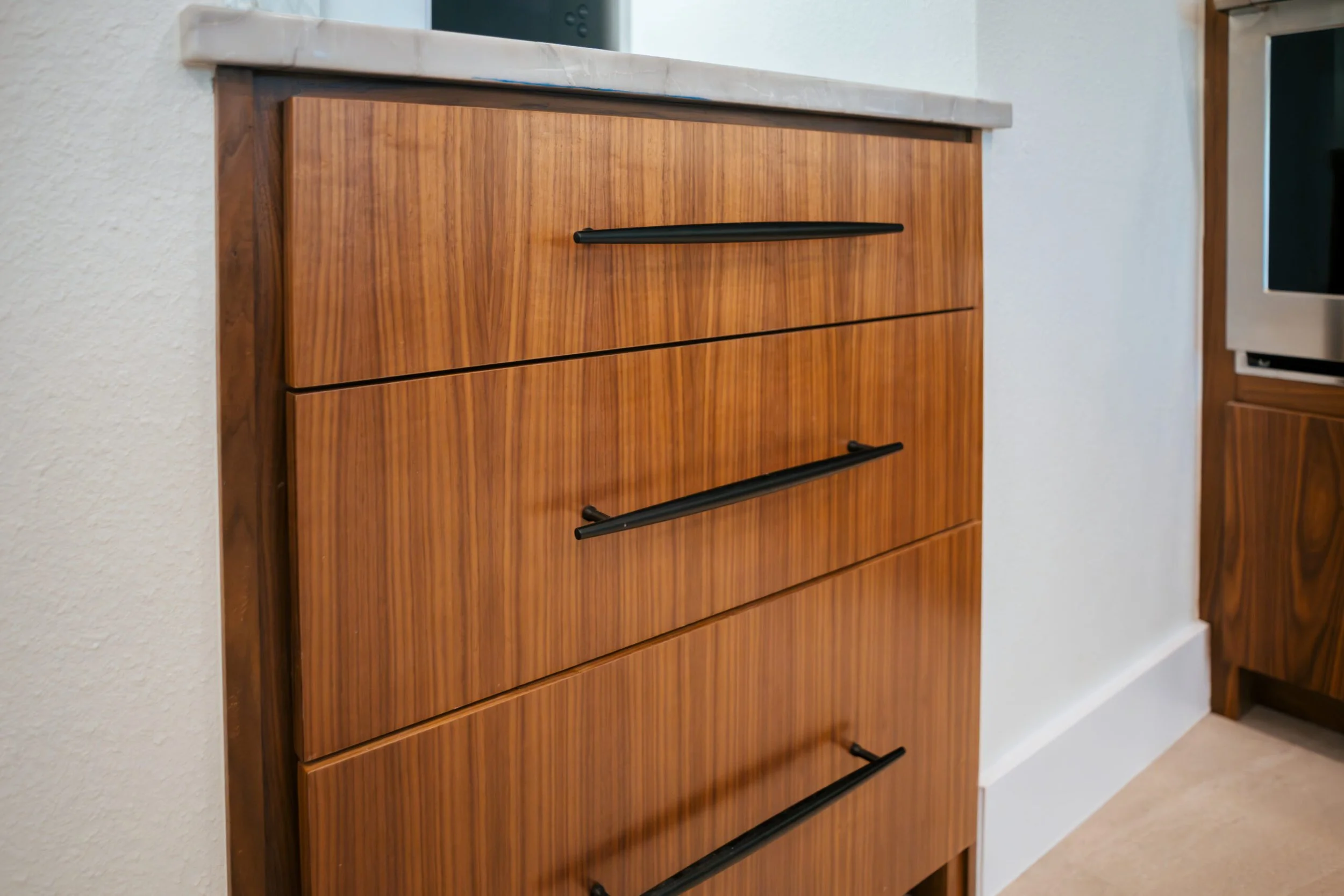 Close-up of a wooden cabinet with black handles, against a white wall in a modern interior.