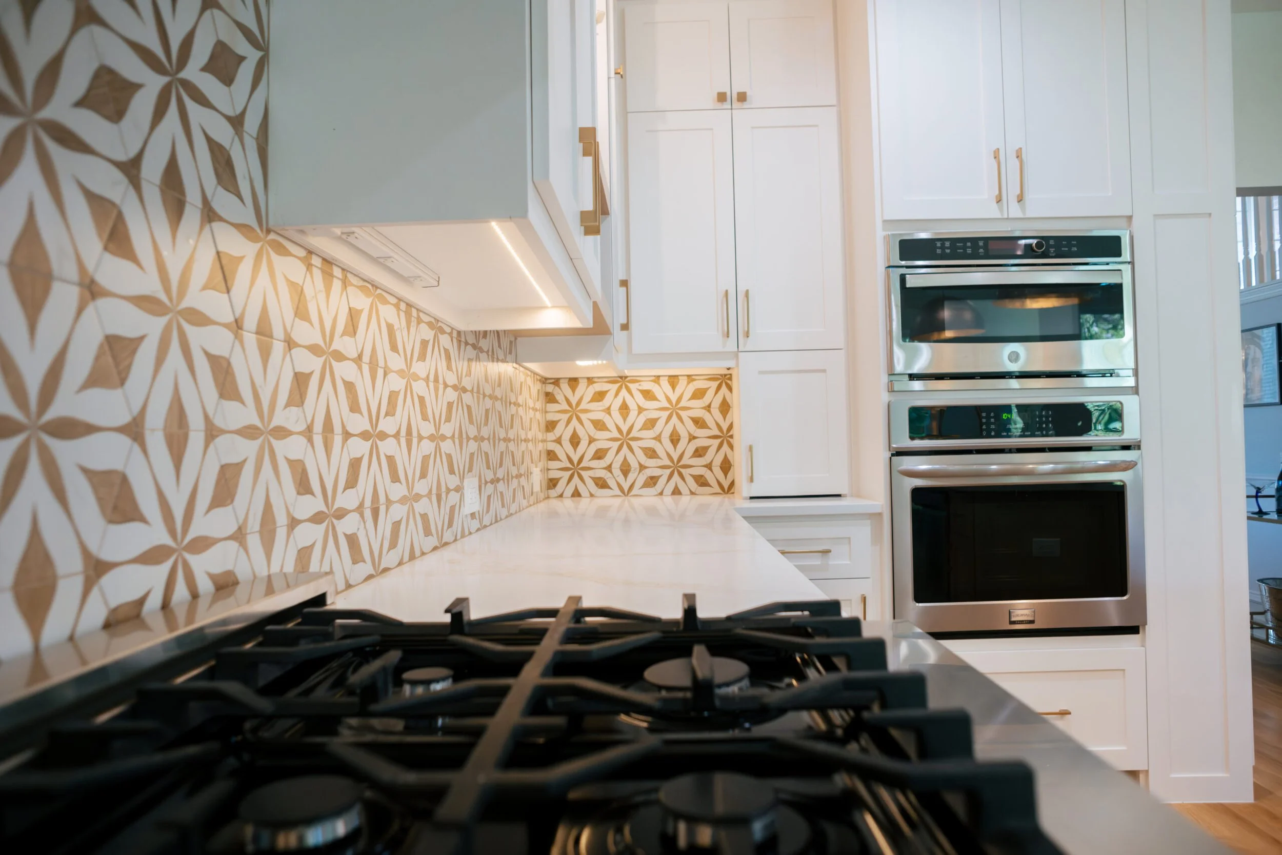 A modern kitchen with white cabinets, stainless steel appliances, a patterned tile backsplash, and a view of a window with blinds.