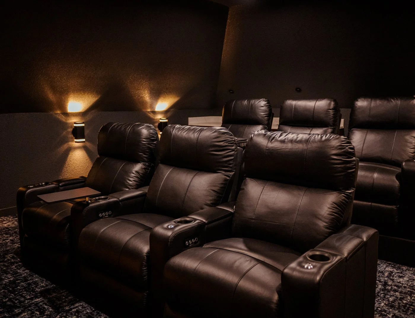 Home theater room with leather recliner seats, dim lighting, and black walls.