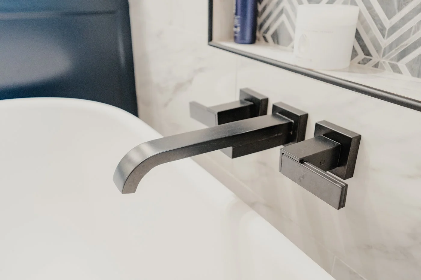 Close-up of a modern wall-mounted black faucet and handle above a white sink in a bathroom.