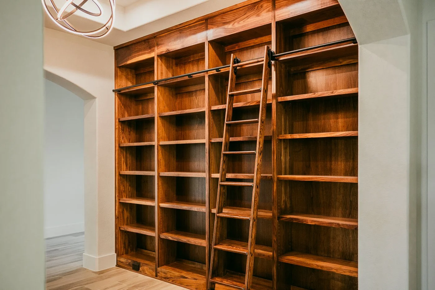 Empty wooden bookshelf with a small ladder in front, inside a well-lit room.